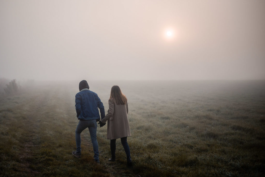 para zakochanych idąca po polu we mgle o wschodzie słońca