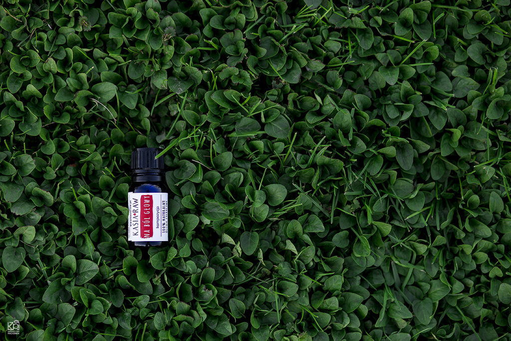 Zdjęcie przedstawia olejek eteryczny położony na zielonej trawie, kompozycja na ból głowy