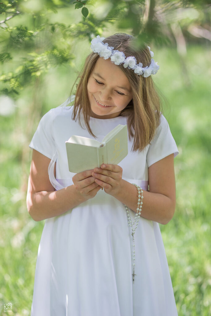 Śmiejąca się Emilka trzyma w ręku białą książeczkę i różaniec