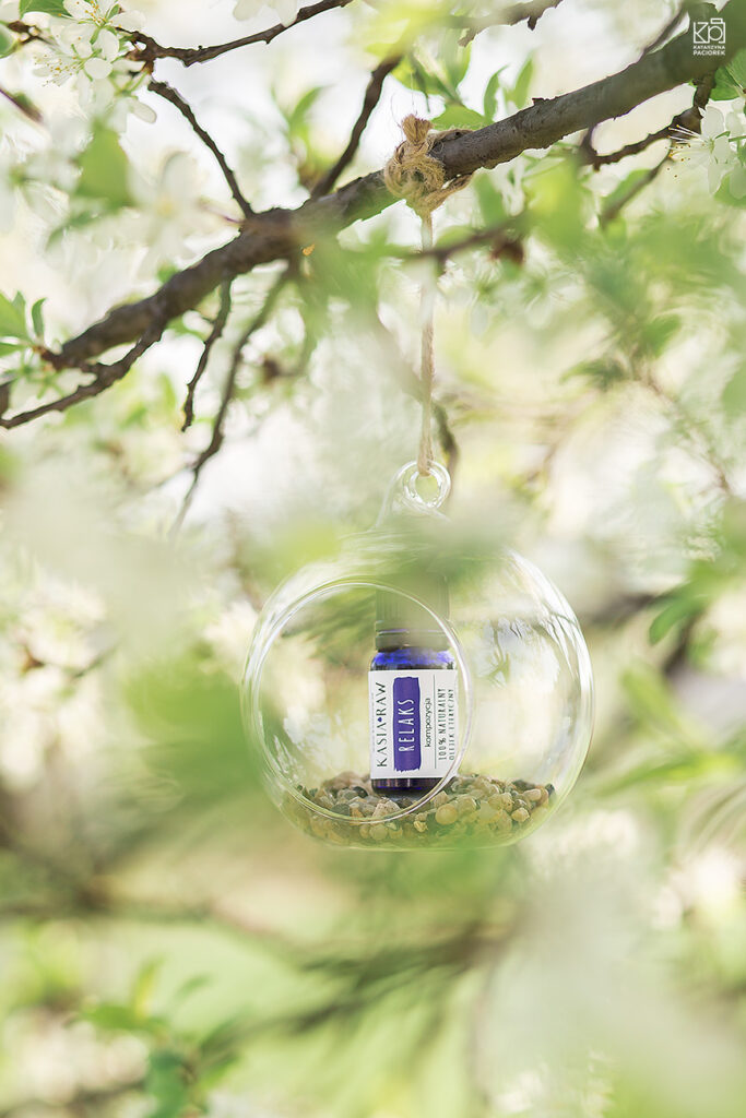 Zdjęcie przedstawia olejek eteryczny umieszczony w szklanej kuli wkomponowanej w liściach, kompozycja na relaks