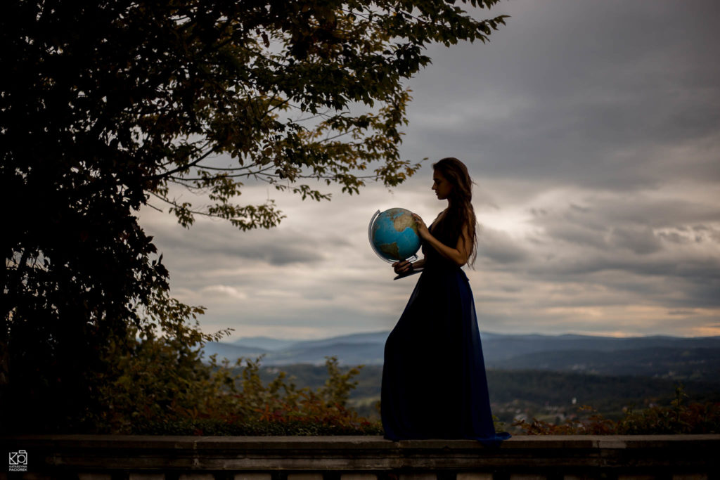 Kobieta w niebieskiej sukni stoi z globusem w ręku