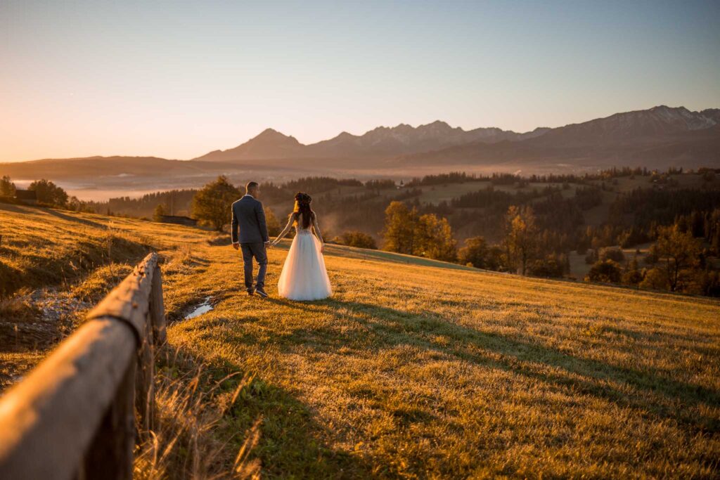 Para ślubna chodzi po łaće o wschodzie słońca, z widokiem na Tatry