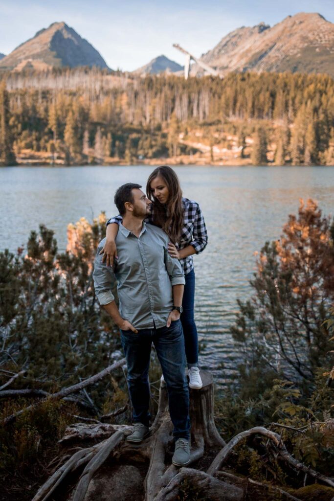 Mąż i żona stojący na pniu przy brzegu jeziora z górami w tle