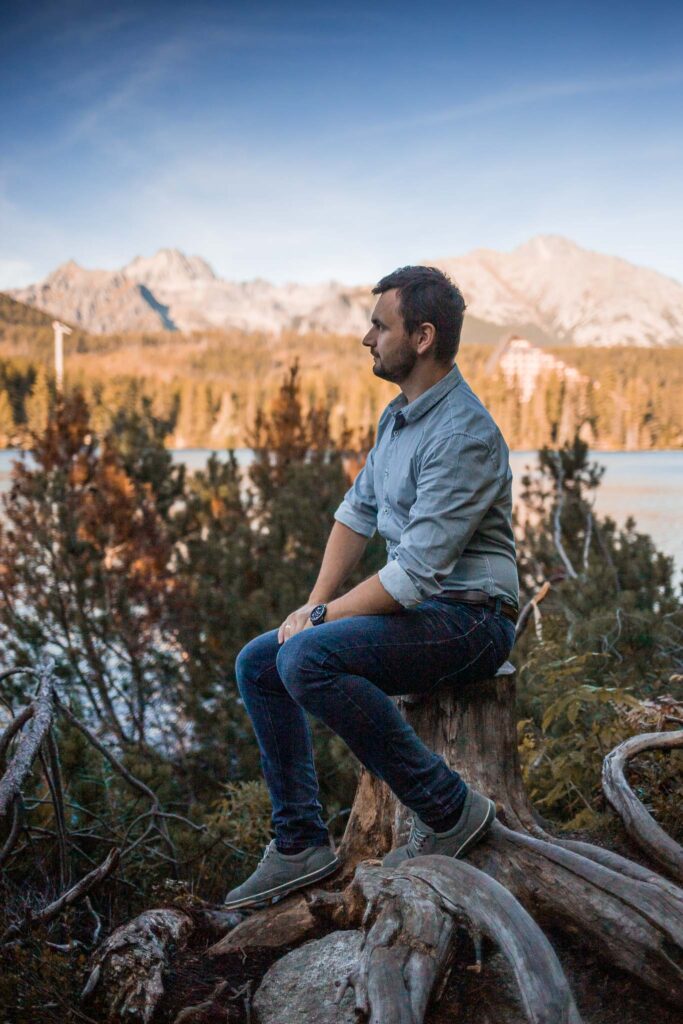 mężczyzna siedzący bokiem, patrzący na jezioro i góry