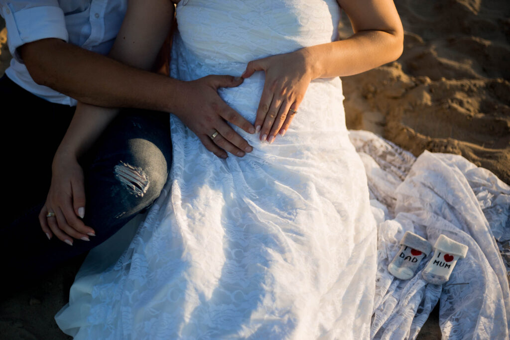 Fotografia przedstawia zbliżenie na ciążowy brzuch, na którym Karolina i Tomek położyli swoje dłonie, tworząc z nich serce.