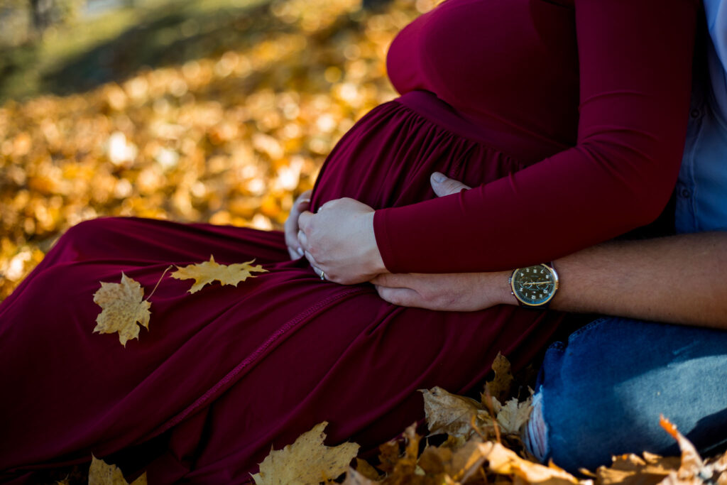 Fotografia przedstawia zbliżenie na ciążowy brzuch, który obejmowany jest przez dłonie.