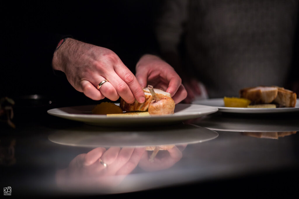 Fotografia przedstawa dłonie kucharza, które układają mięso na talerzu.